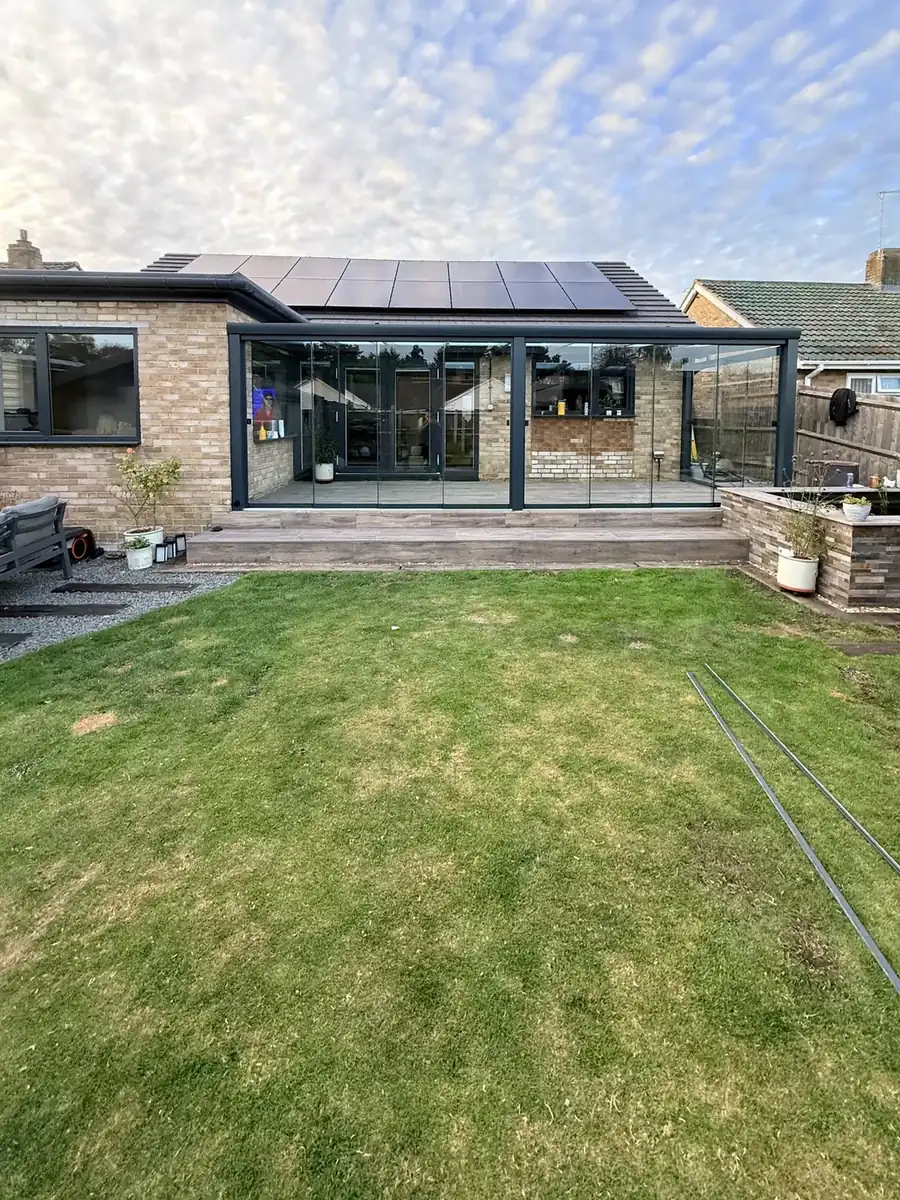 Bungalow with solar panels and the full-width glass room, seen from the end of the garden