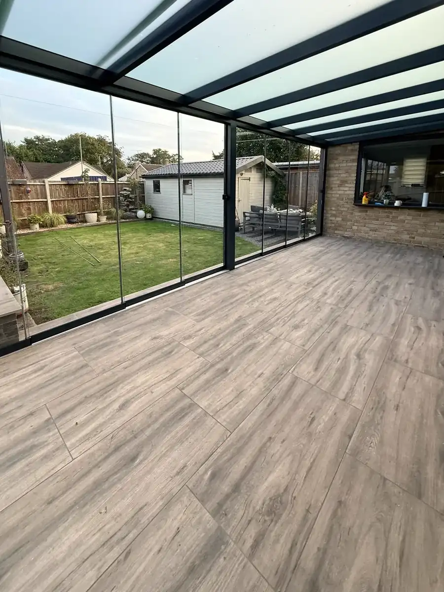 Inside the glass room: wood-effect floor, glass roof and a view of the garden