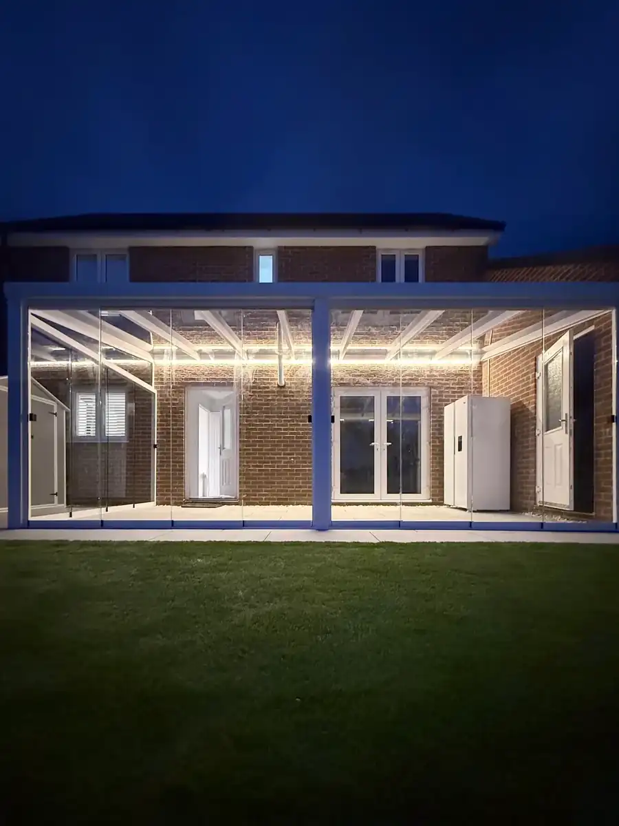 White glass room glowing at night, seen from the end of the garden