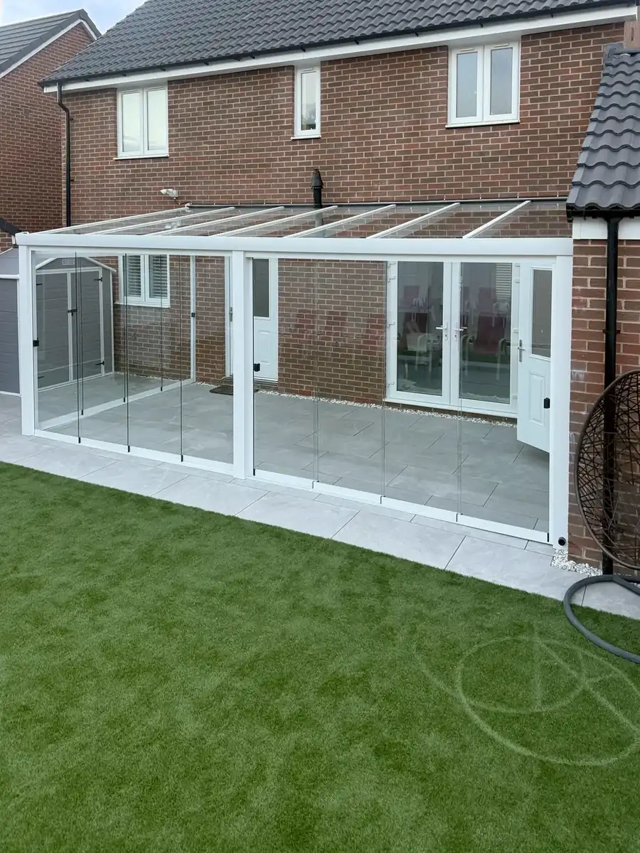 White glass room with clear glass roof panels, seen from the edge of the lawn